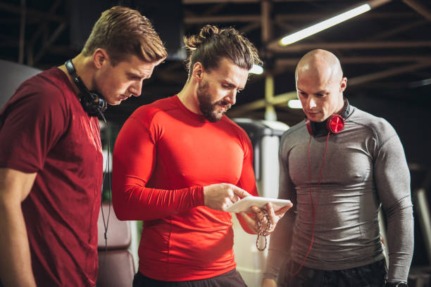 Three men in sportswear discuss something on a tablet, highlighting fitness facilities at Emaar Valley Phase 2.