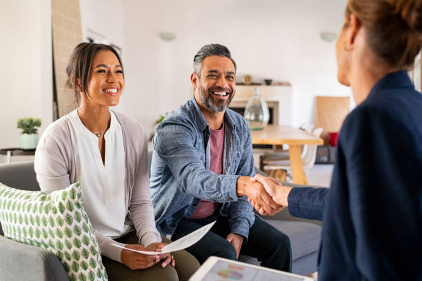 A couple is sitting on a couch, smiling, and shaking hands with a professional.