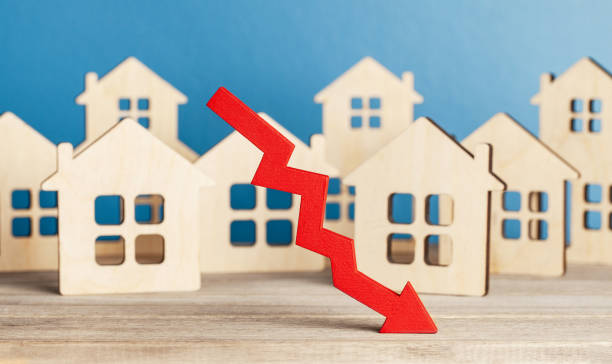 A red downward arrow in front of wooden house cutouts symbolizes a decline in the housing market.